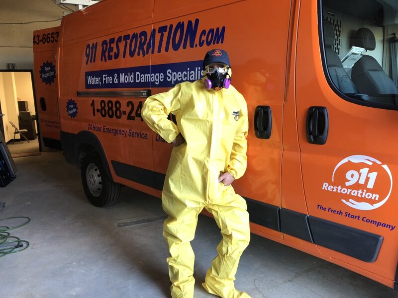 water restoration tech wearing a hazmat suit standing next to a 911 Restoration work van